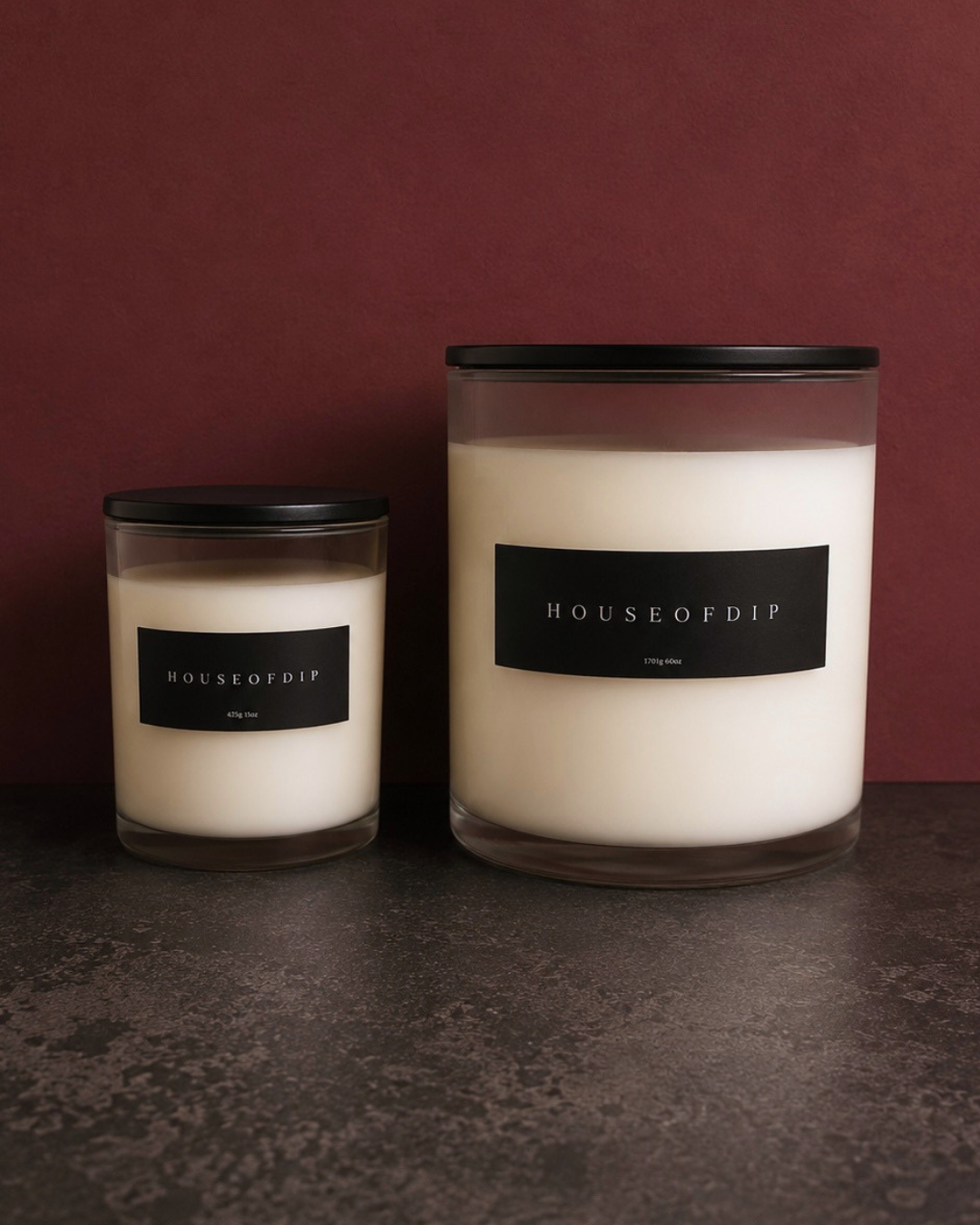 Two candles with 'HOUSEOFDIP' labels on a dark surface and maroon background